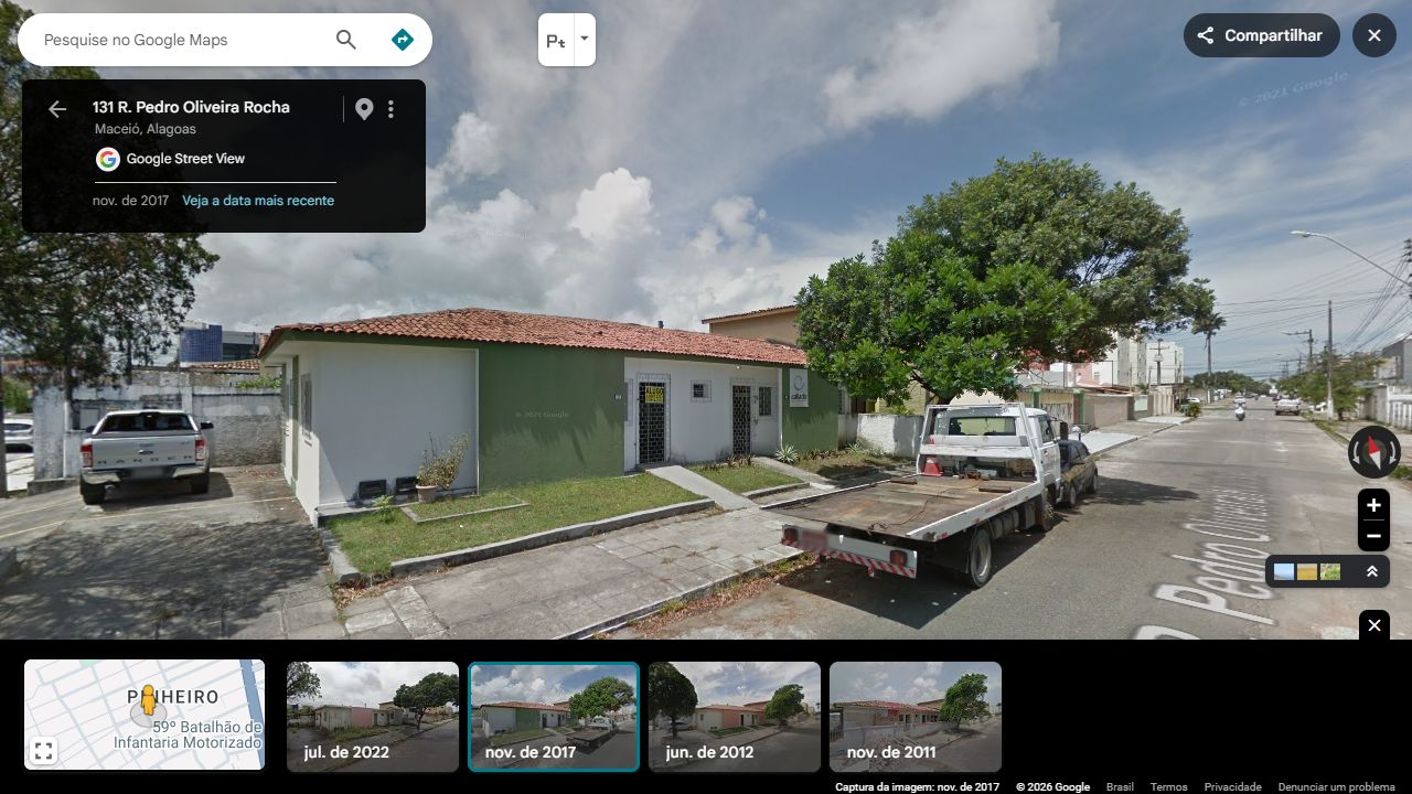 Frente inteira: painéis verdes, trecho branco, dois acessos gradeados, janelas e telhado cerâmico.