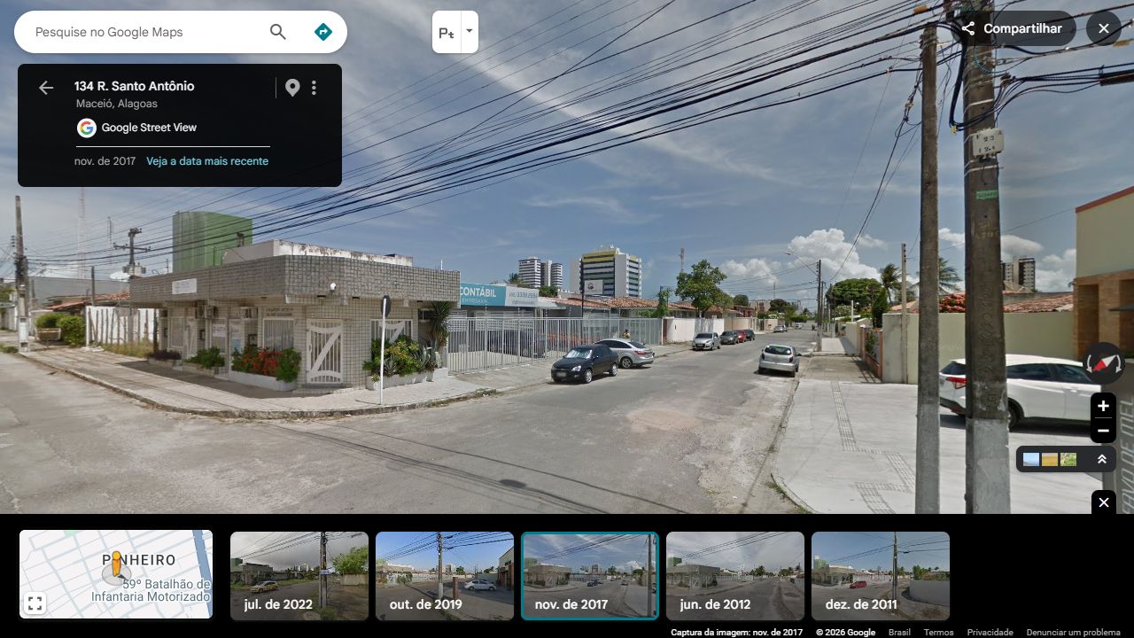 Esquina oposta à casa verde: fachada revestida, volume superior verde, sequência de grades brancas e letreiro Contábil Empresarial. Duas torres aparecem distantes, sem identificação de seus lotes.